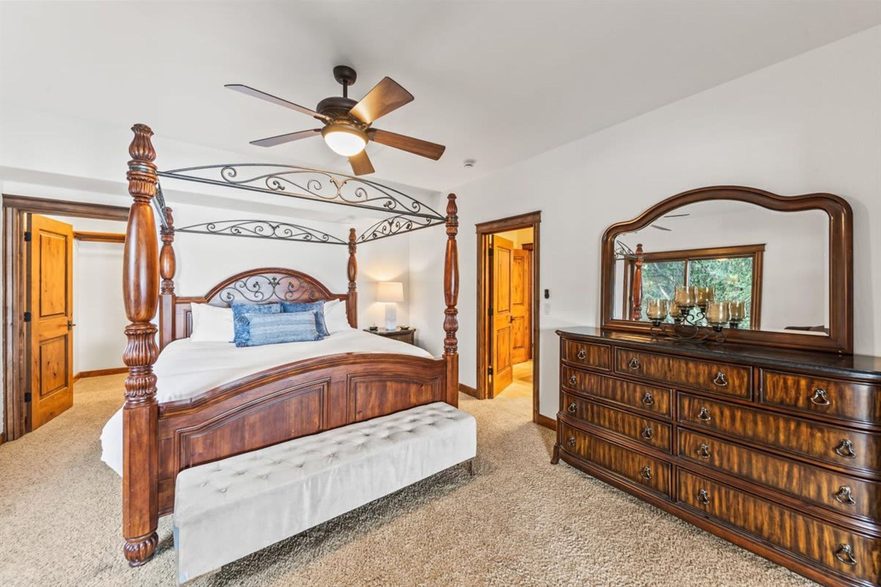 Un lit à baldaquin avec un ventilateur de plafond, une commode en bois et un grand miroir.