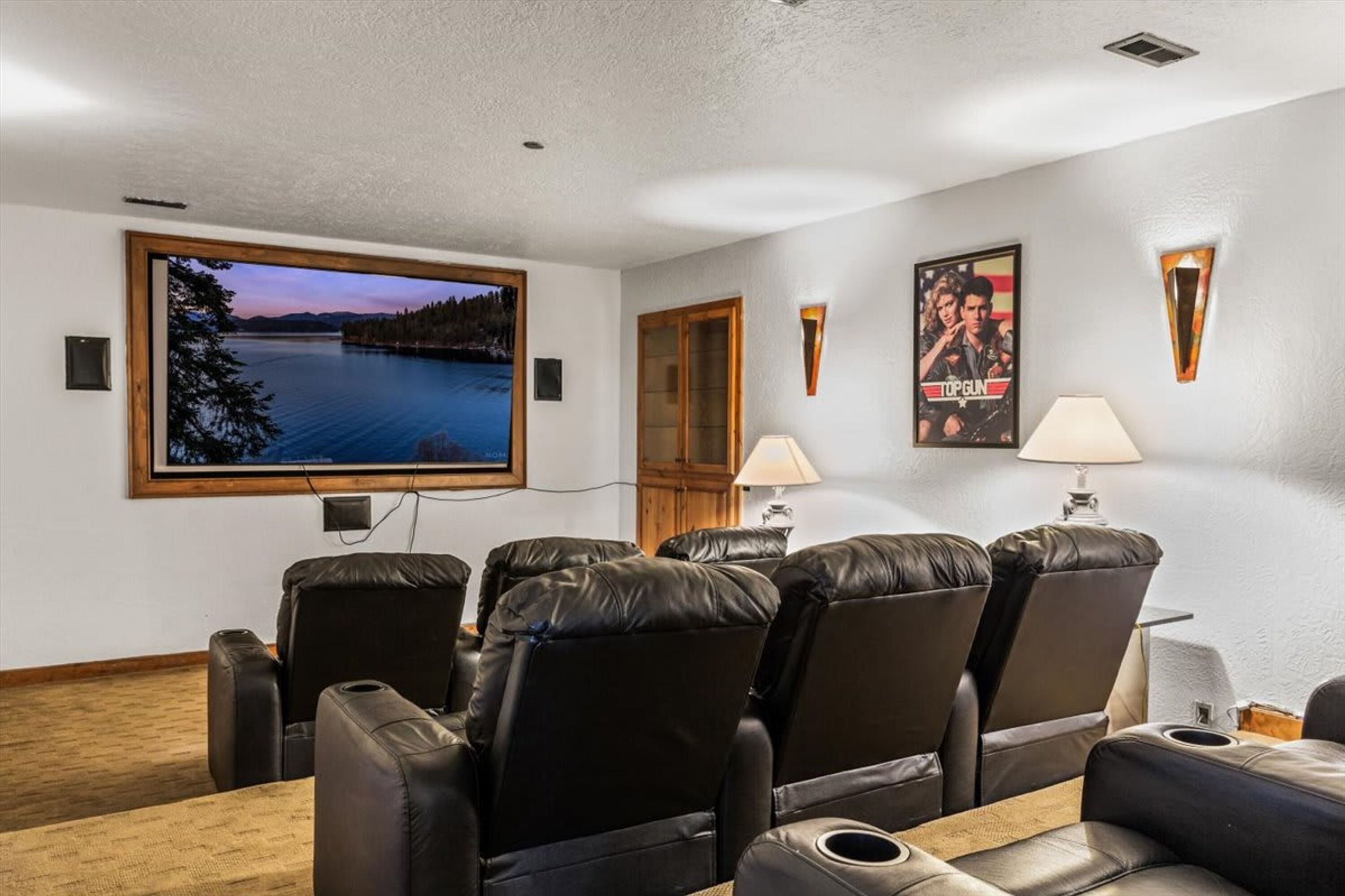 Une salle de cinéma privée équipée d’un grand écran, de fauteuils inclinables, de lampes fixées au mur et de posters encadrés.