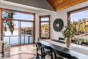 A dining area with a table, chairs, and a view of a lake and forest.