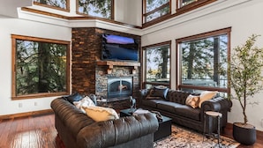 A modern living room with a stone fireplace, leather sofas, large windows, and a flat-screen TV. - Deja View in Hayden With 5 Bedrooms and 6 Bathrooms (Hayden)