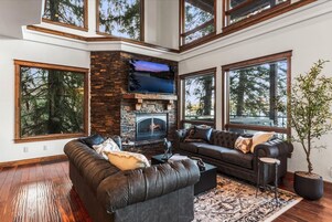 Una sala de estar moderna con chimenea de piedra, sofás de cuero, ventanas grandes y un televisor de pantalla plana.