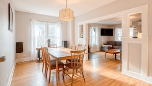 Amplia sala de estar con mesa de comedor de madera, sillas, un sofá y una televisión.