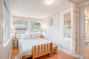 A bedroom with a wooden bed, a window with a view, a bedside table with a lamp, and a door leading to another room. - Parkside Downtown Coeur d Alene (Coeur d'Alene)
