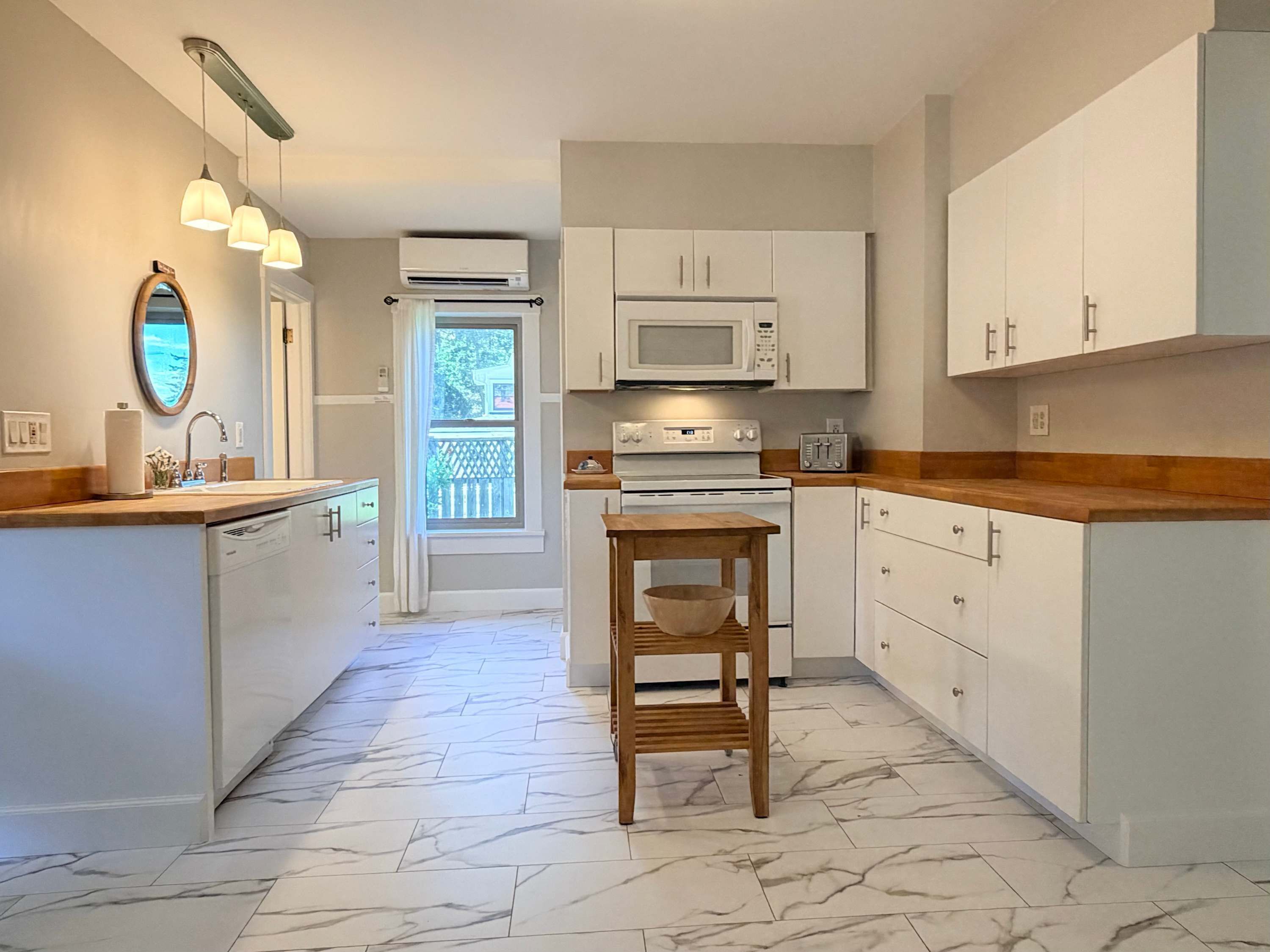 A kitchen with white cabinets, a microwave, a wooden table, and a view of the outdoors through a window.