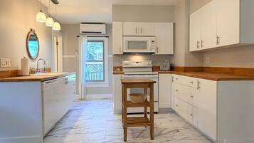 A kitchen with white cabinets, a microwave, a wooden table, and a view of the outdoors through a window.