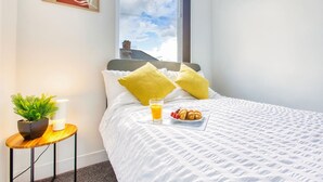 A neatly made bed with a white duvet, two yellow pillows, a bedside table with a plant, a glass of orange juice, and a plate of croissants. - Modern 3-bed Home Sleeps 6 With Parking Fast Wifi Perfect for Contractors Long Stays (St Helens)