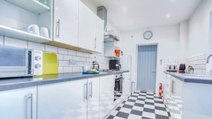 A modern kitchen with white cabinets, a black and white checkered floor, a coffee machine, and a clock on the wall. - Modern 3-bed Home Sleeps 6 With Parking Fast Wifi Perfect for Contractors Long Stays (St Helens)