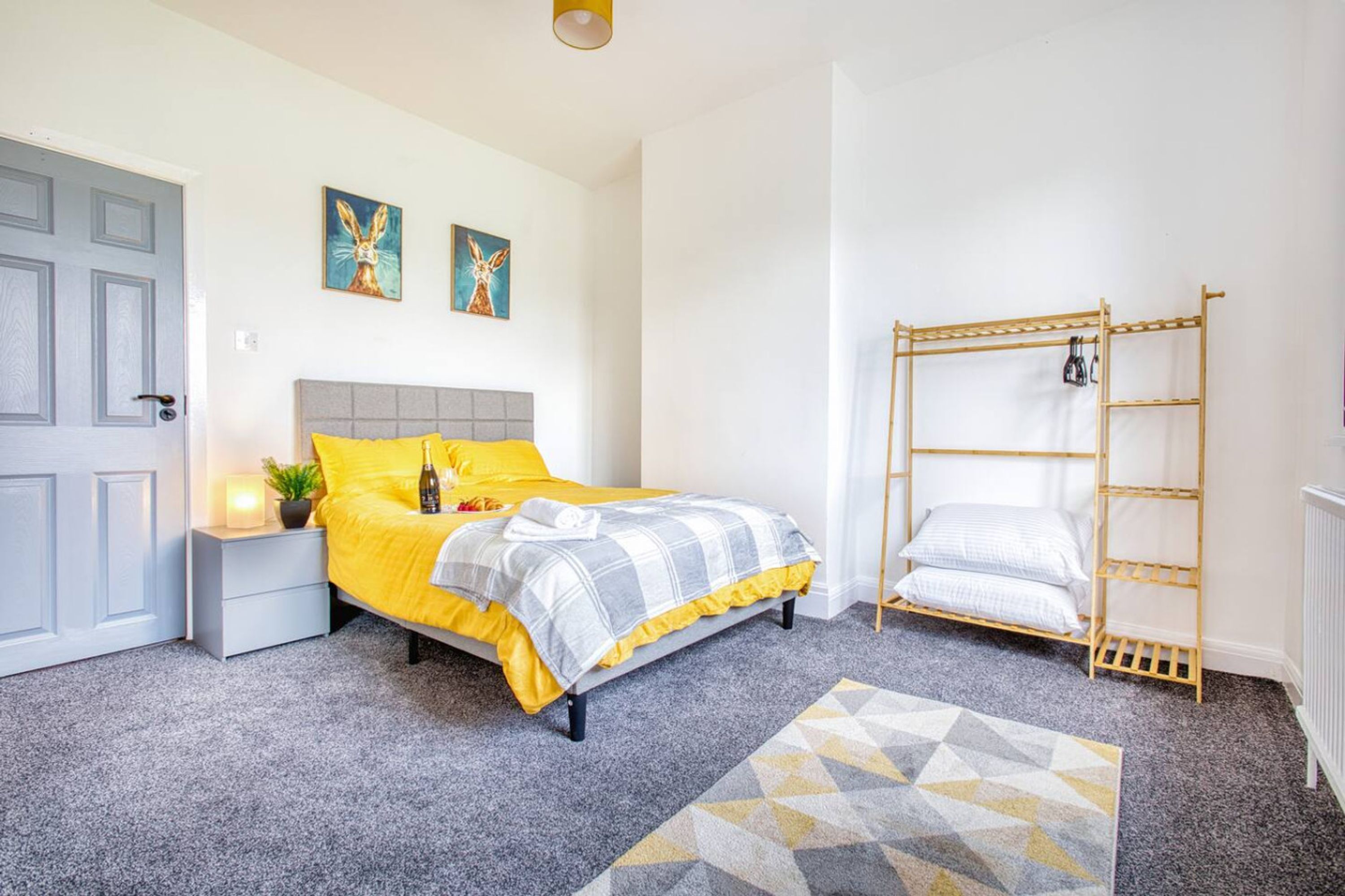 A bedroom with a bed, a bedside table, a lamp, a wall-mounted shelf, and a door.