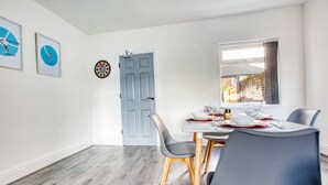 A dining area with a table set for four, a dartboard, and framed artwork on the wall. - Modern 3-bed Home Sleeps 6 With Parking Fast Wifi Perfect for Contractors Long Stays (St Helens)