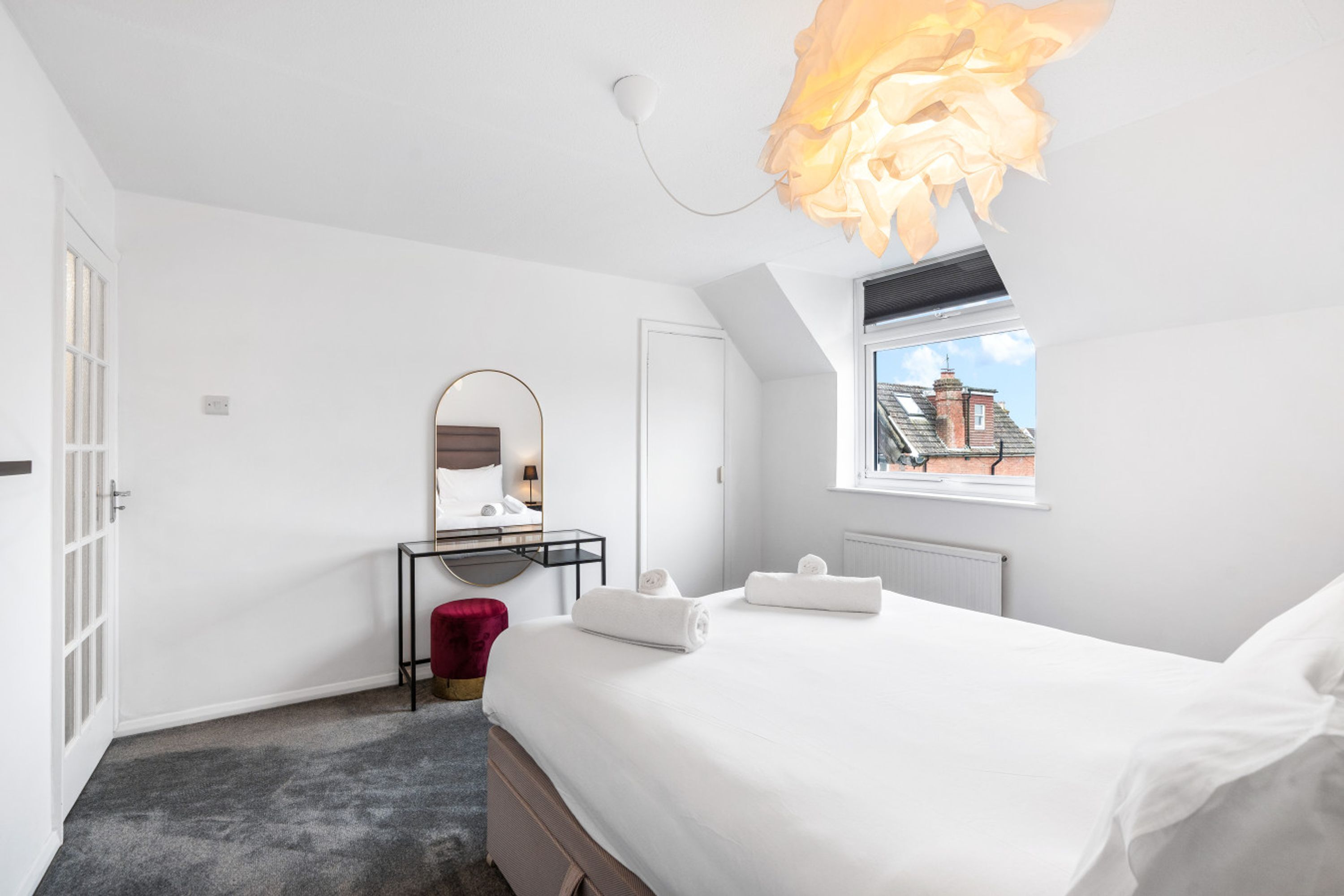 A bedroom with a bed, a mirror, a vanity, and a window with a view of buildings.
