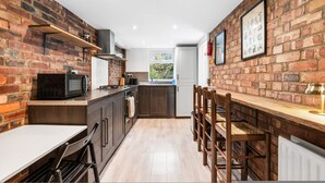 A kitchen with brick walls, wooden cabinets, a microwave, and a dining area with chairs. - Central Horsham 5BR Home Parking Pets Allowed (Horsham)