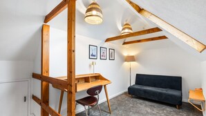 A loft bedroom with a wooden desk, a dark sofa, and two wall-mounted lamps. - Central Horsham 5BR Home Parking Pets Allowed (Horsham)