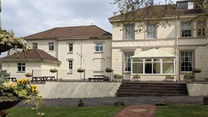A two-story building with a covered entrance, a paved driveway, and a small garden area with flowers. - Room 2 Manor Park Country House in Swansea (Swansea)