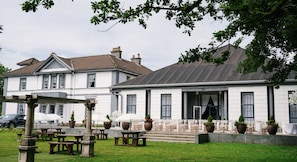 A building with a white facade, large windows, and a covered outdoor seating area with tables and umbrellas. - Room 5 - Manor Park Country House Wales (Swansea)