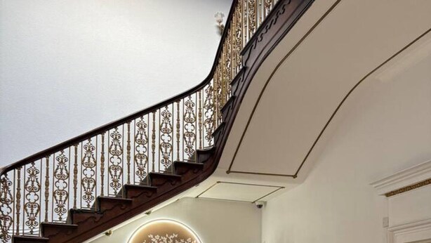 Una imponente escalera con barandillas ornamentadas, un elemento circular en la pared y arreglos florales.