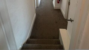 Un pasillo estrecho con pisos alfombrados, paredes blancas y una lámpara en el techo.