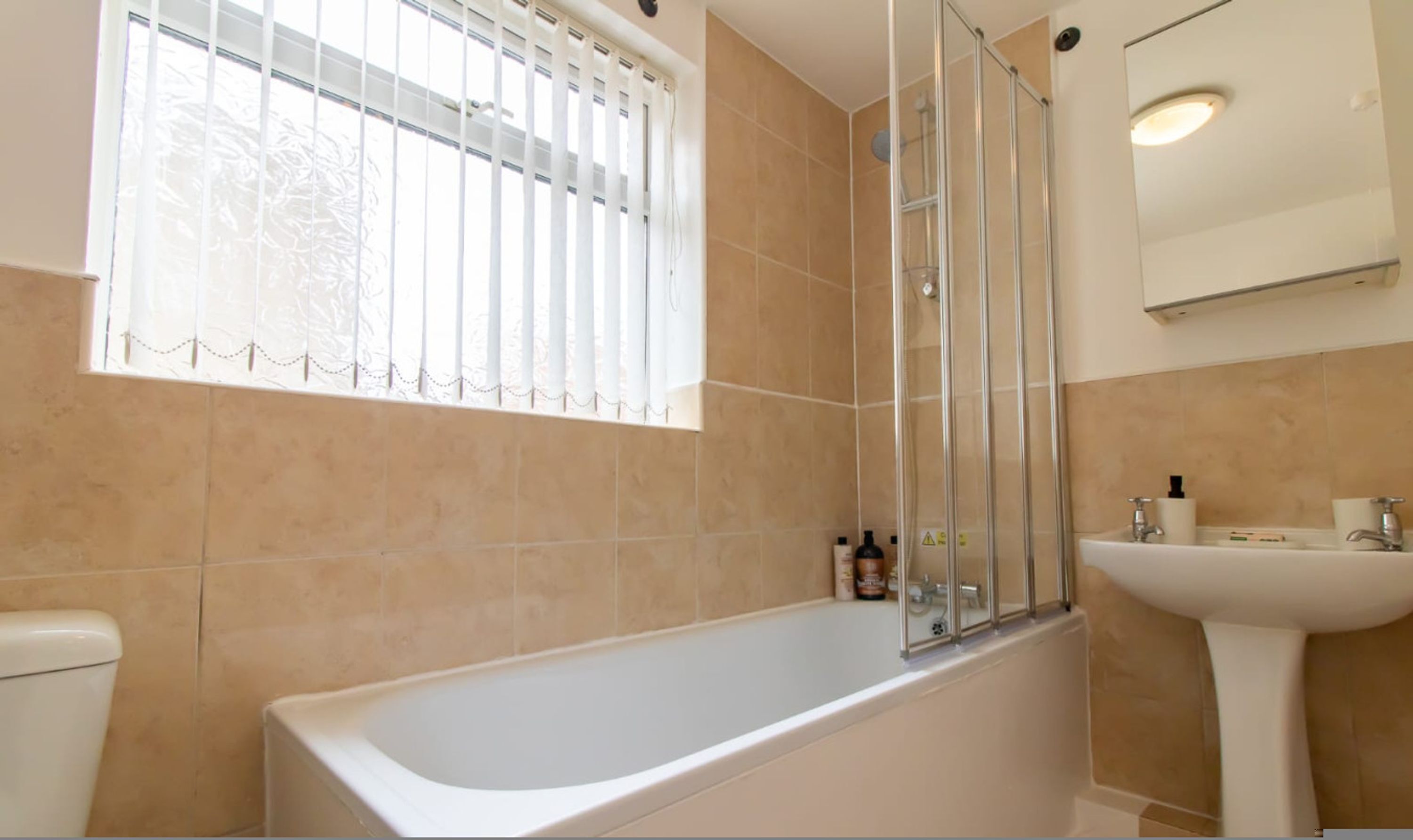 A bathroom with a bathtub, a shower enclosure, a sink, and a window with blinds.