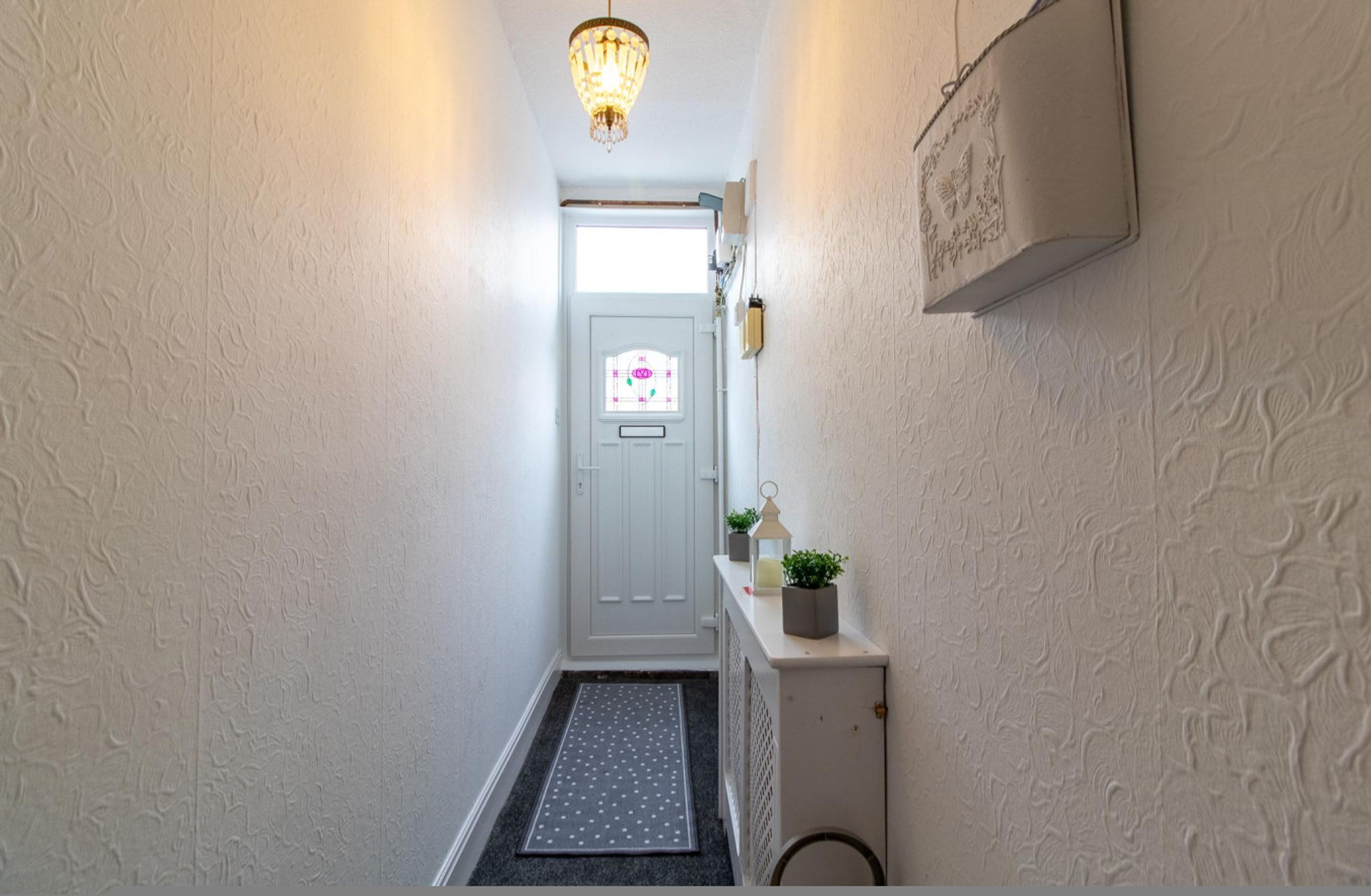 A narrow hallway with a door at the end, a small step leading to a landing, and a wall-mounted light fixture above.