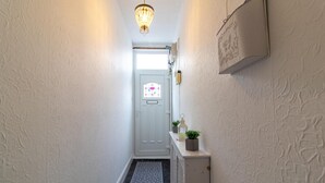 A narrow hallway with a door at the end, a small step leading to a landing, and a wall-mounted light fixture above. - Alice Street Retreat - 1BR Sleeps 4 Street Parking (South Shields)