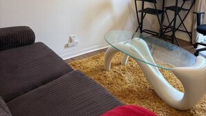 Een woonkamer met een bank, een glazen salontafel, een eettafel met stoelen en een wandklok.