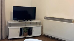 Een woonkamer met een flatscreen televisie op een witte tv-meubel, een witte radiator en een witte stoel.