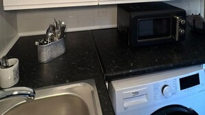 Een keuken met witte kastjes, een magnetron, een broodrooster en een wasmachine.