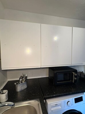 A kitchen with white cabinets, a microwave, a toaster, and a washing machine. - Cozy Northolt Hideaway 1BR Free Wifi Streetparking (Northolt)
