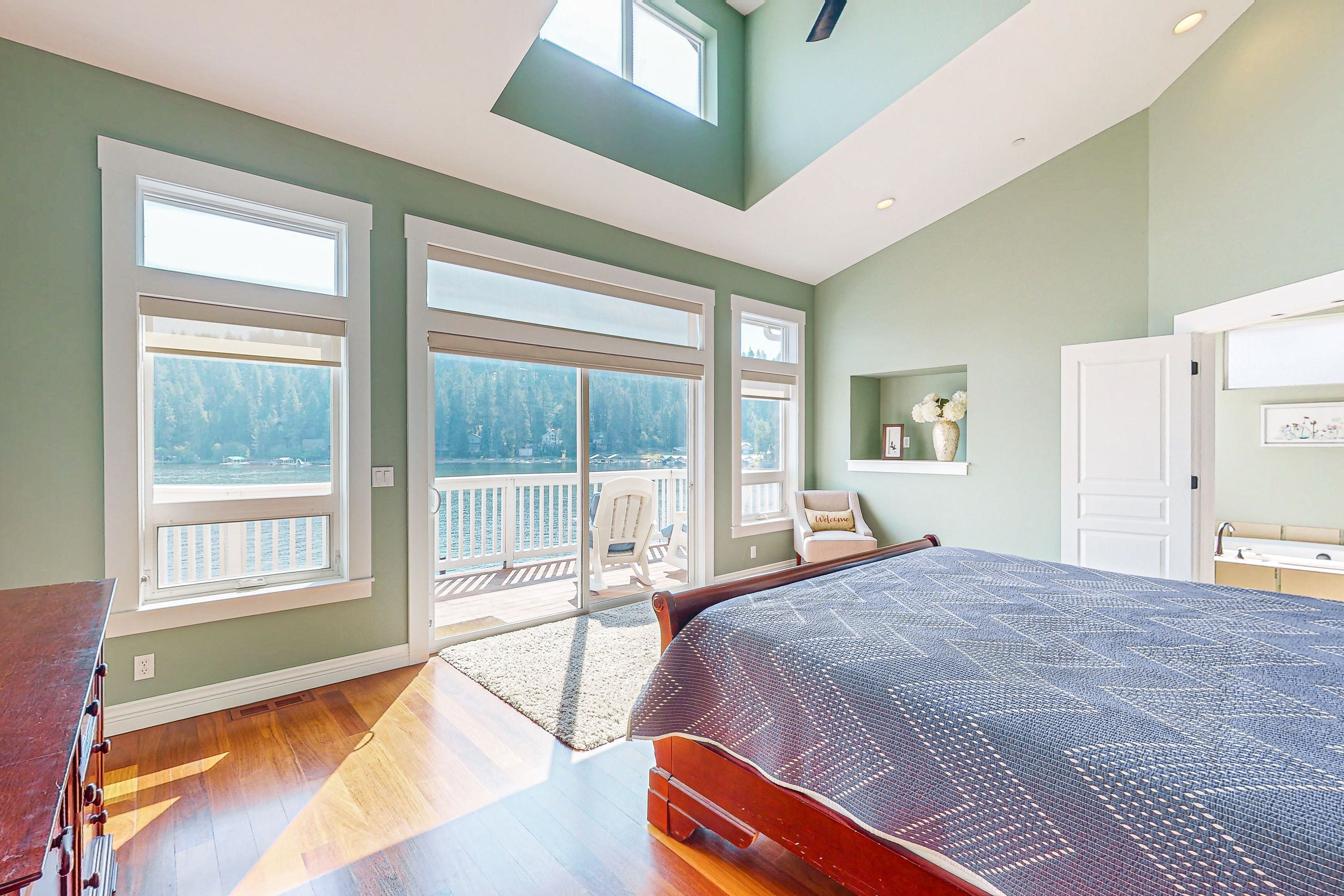 A bedroom with a large bed, a skylight, a balcony with a view, and a bathroom with a sink.