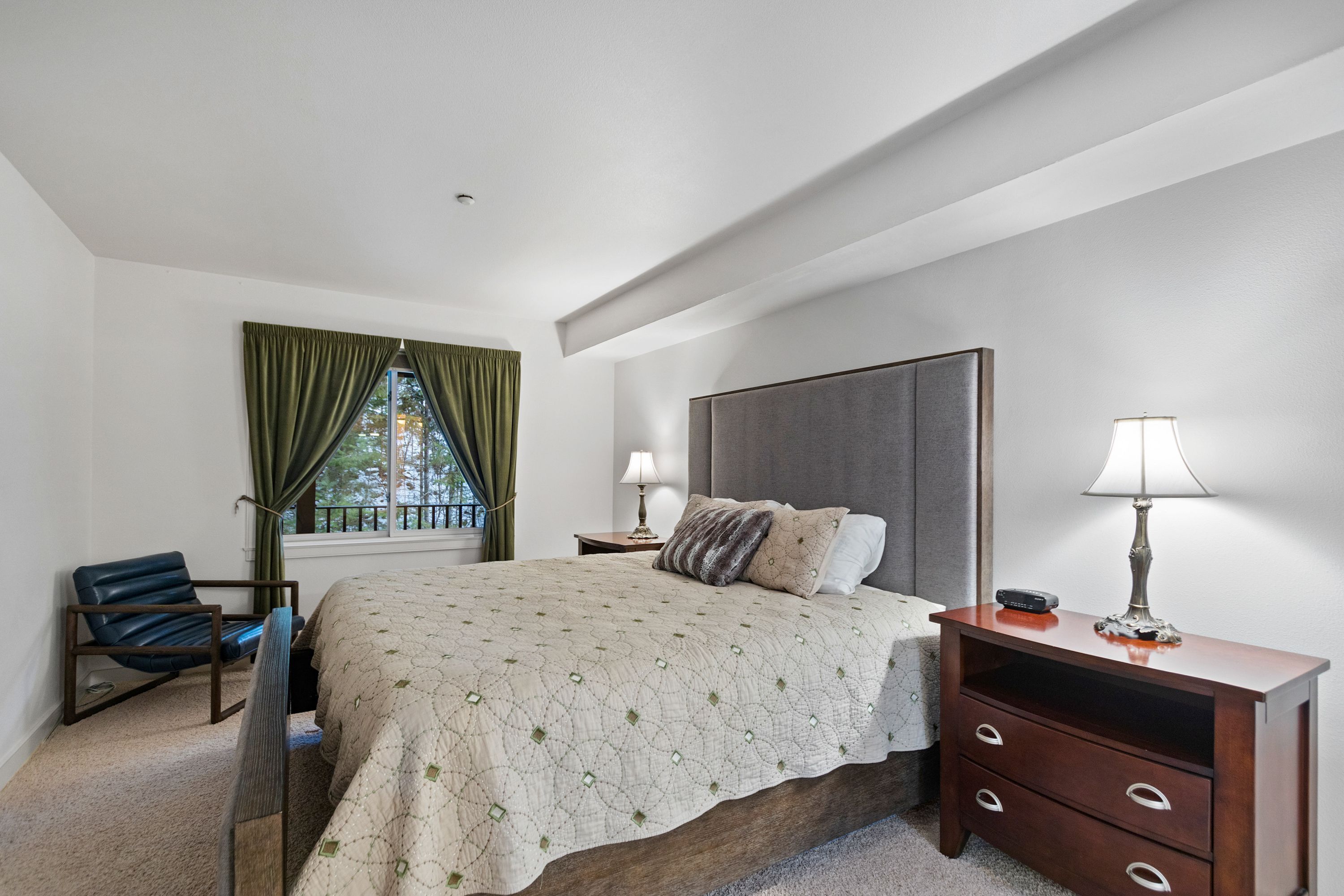 A bedroom with a bed, a chair, a nightstand, a lamp, and a window with curtains.