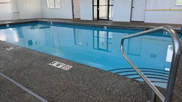 An indoor swimming pool with a clear water surface, marked depth lines, and a metal pool ladder.