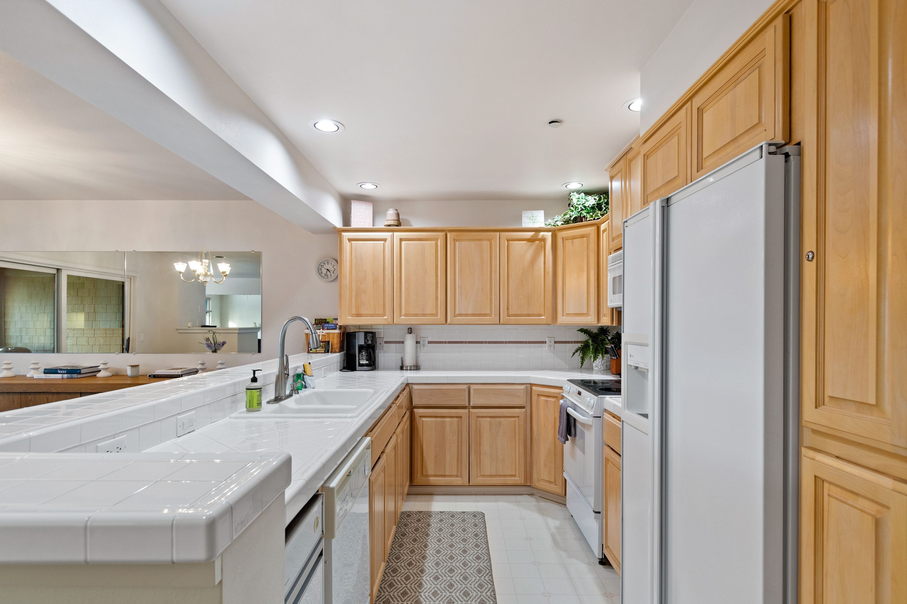 A modern kitchen with wooden cabinets, a white countertop, a built-in oven, and a refrigerator.