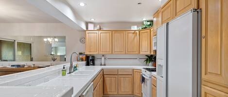 A modern kitchen with wooden cabinets, a white countertop, a built-in oven, and a refrigerator.