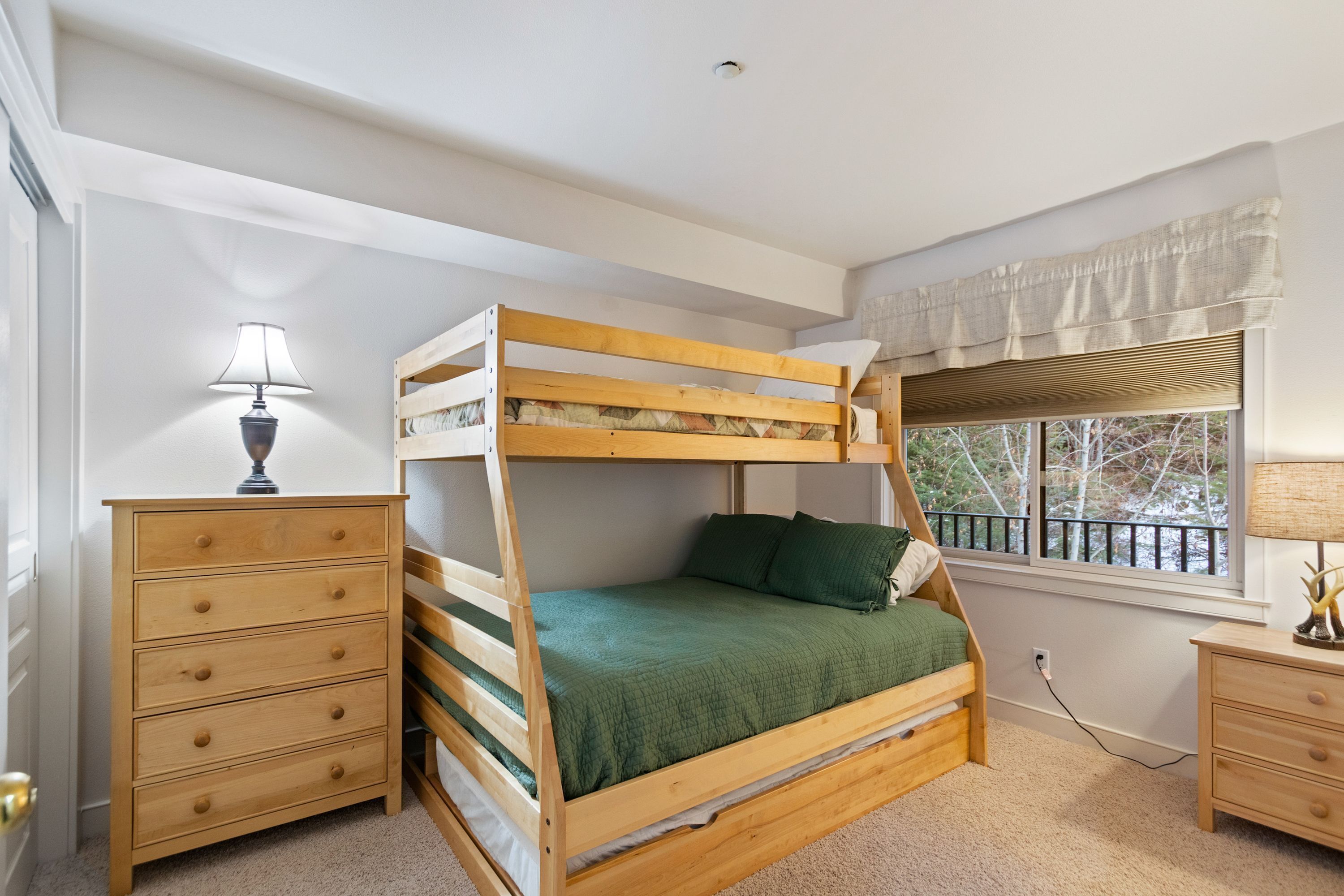 A bunk bed with a green bedspread, a wooden dresser, and a nightstand with a lamp.