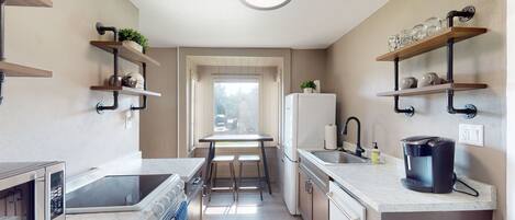 A compact kitchen with a built-in oven, microwave, coffee maker, and a window overlooking a street.