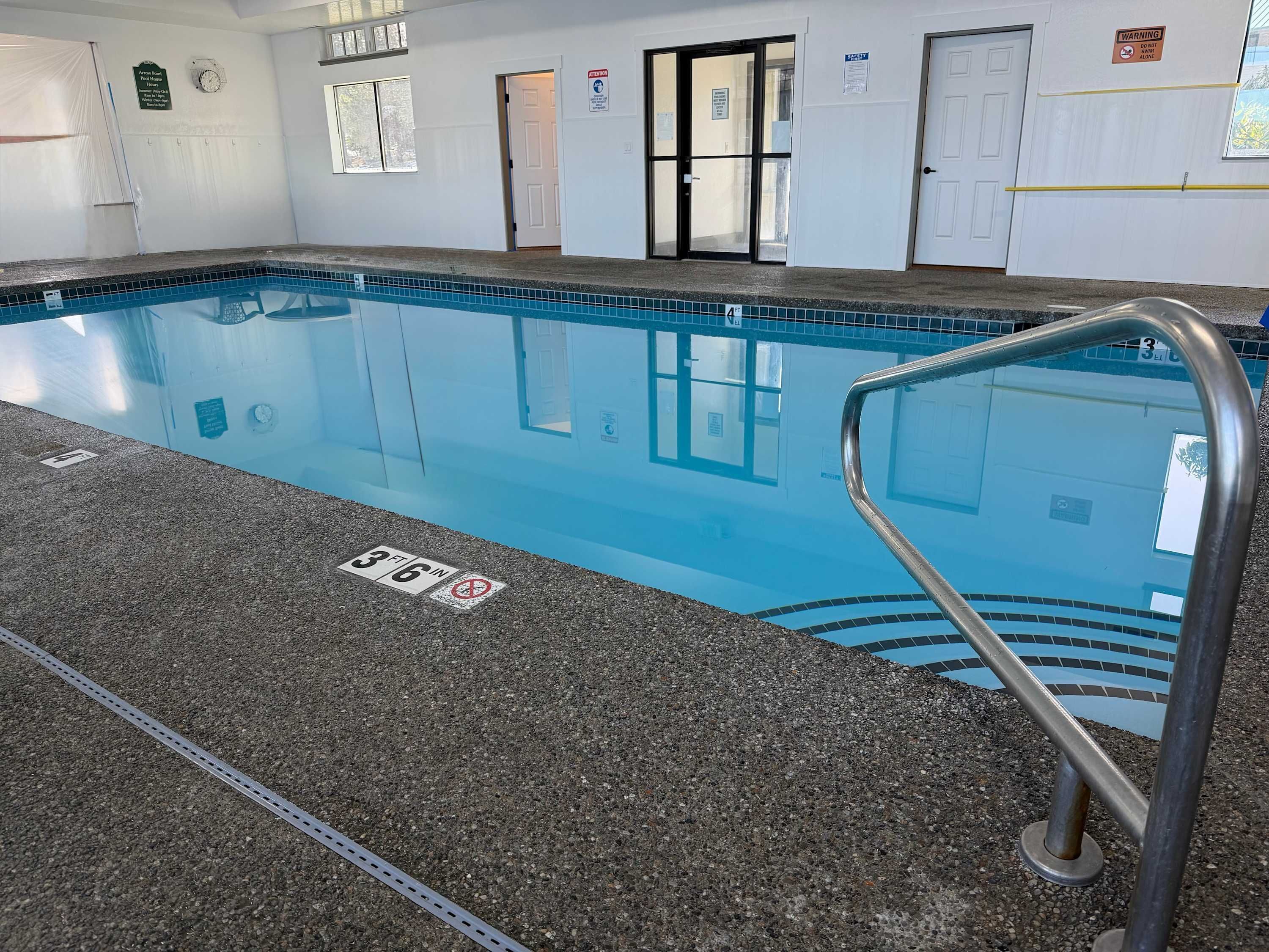 Une piscine intérieure à l’eau claire, avec des repères indiquant la profondeur et un escalier métallique.