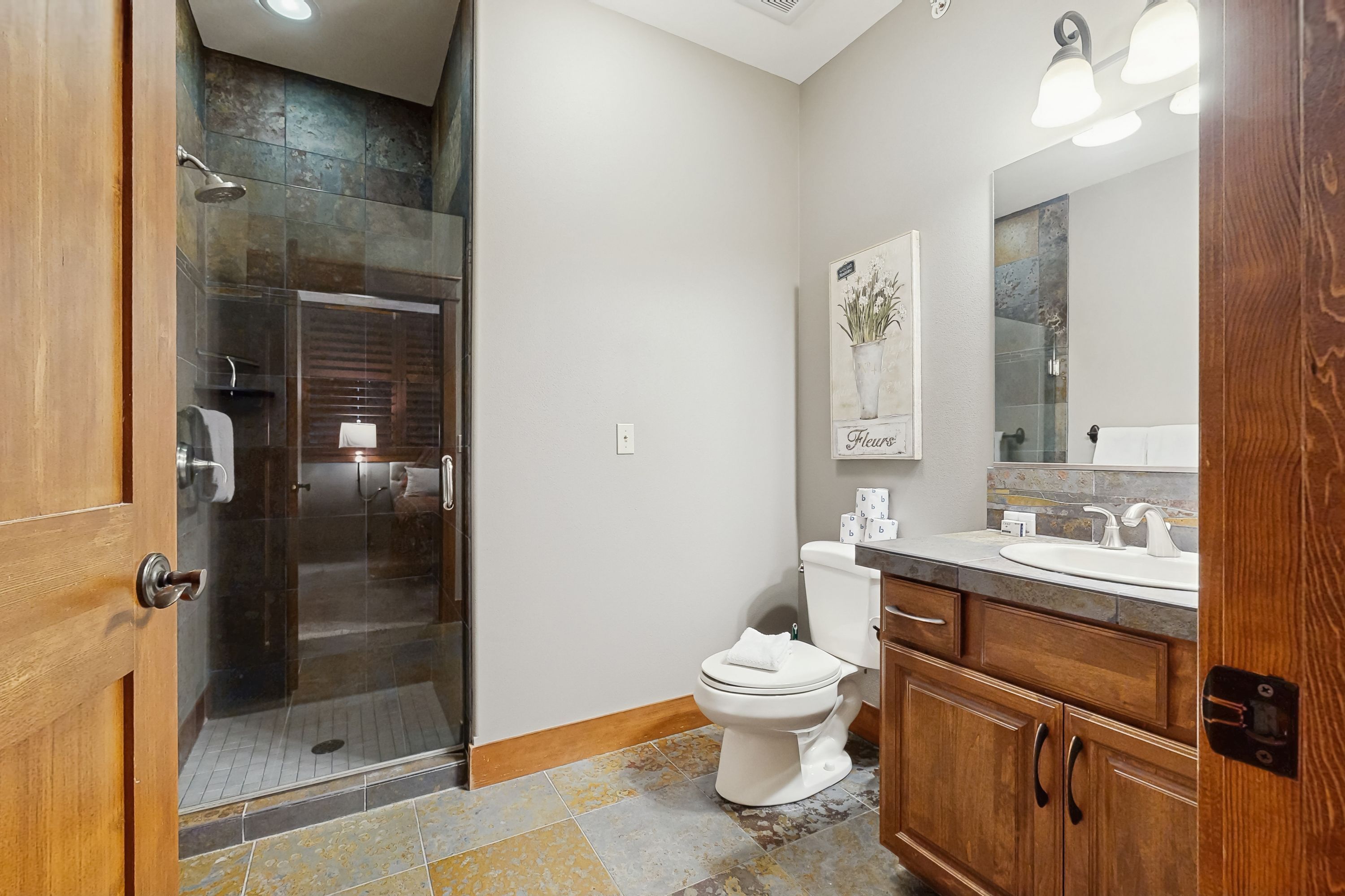 A bathroom with a glass-enclosed shower, a toilet, and wooden cabinets.