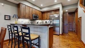 A kitchen with wooden cabinets, a central island with bar stools, a microwave, and a refrigerator. - Fabulous Riverstone Retreat (Coeur d'Alene)