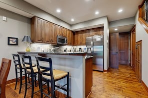 A kitchen with wooden cabinets, a central island with bar stools, a microwave, and a refrigerator. - Fabulous Riverstone Retreat (Coeur d'Alene)