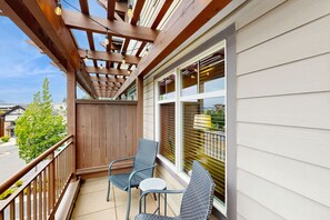 A balcony with wooden railings, two wicker chairs, a small round table, and a pergola with hanging lights. - Fabulous Riverstone Retreat (Coeur d'Alene)