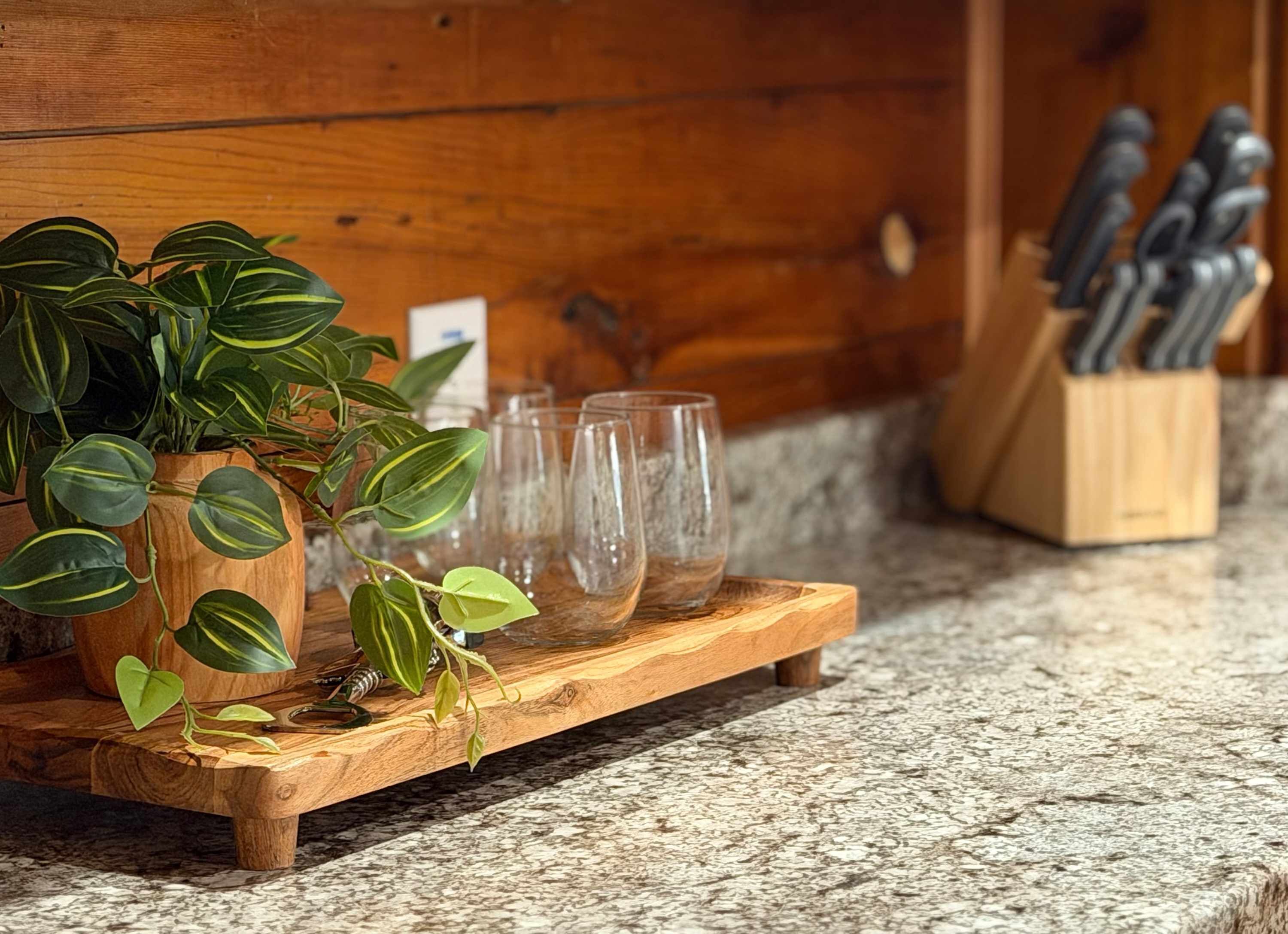 A wooden tray with a potted plant and empty glasses on a granite countertop.