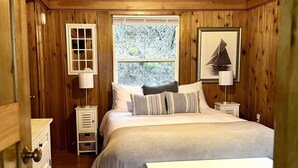 A wooden-paneled bedroom with a bed, bedside tables, a window, and a dresser. - Lakeside Cabin in Hayden (Hayden)