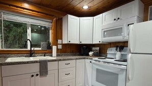 A kitchen with white cabinets, a granite countertop, a sink, a stove, and a refrigerator. - Lakeside Cabin in Hayden (Hayden)