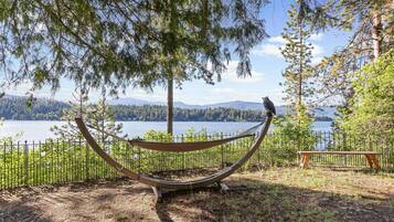 A hammock with a bird perched on it, a bench, and a fenced area with a lake and mountains in the background.