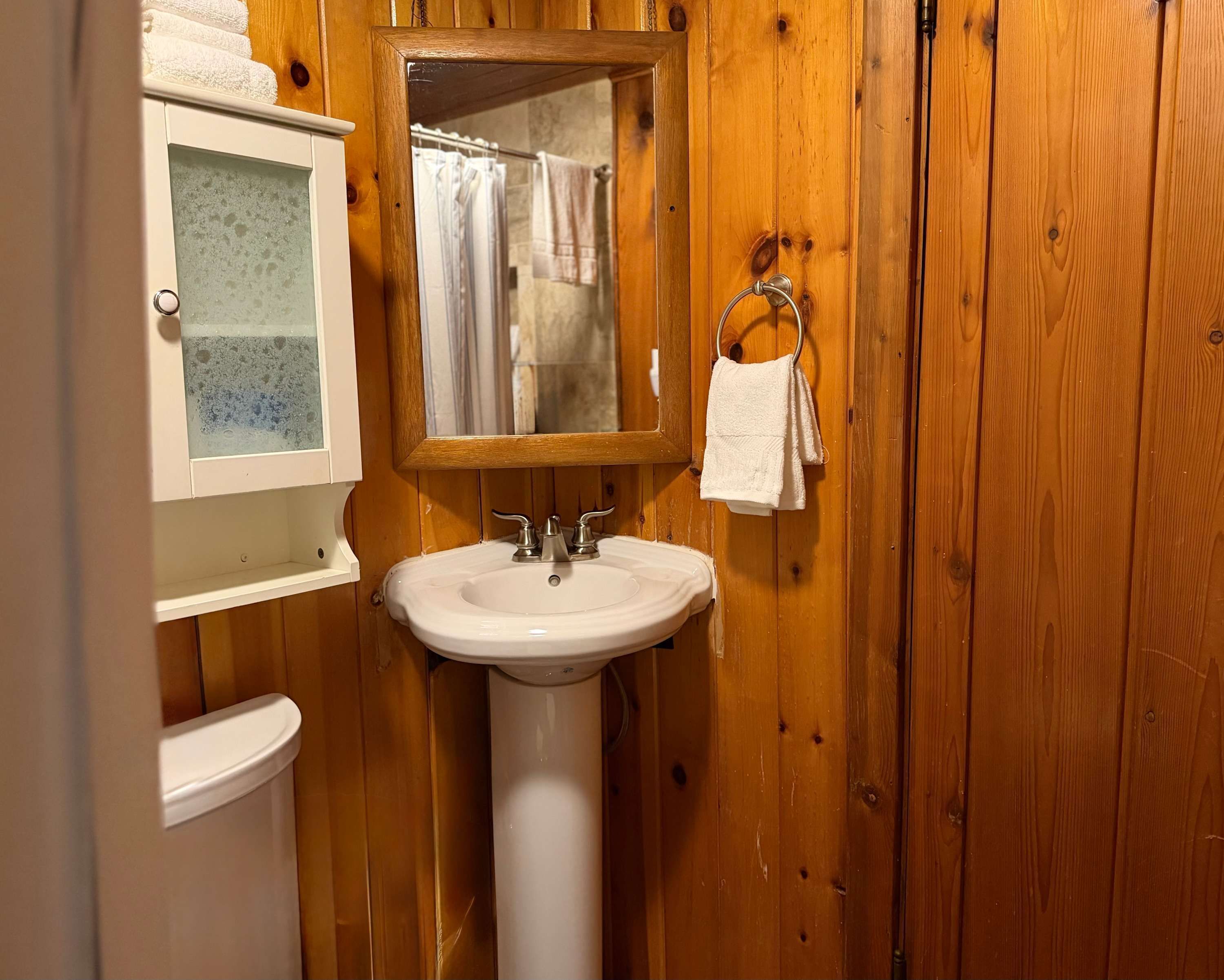 A bathroom with wooden walls, a white sink, a mirror, and a towel rack.