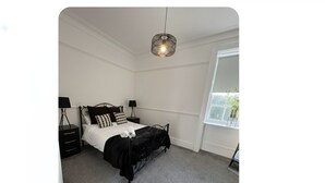 A bedroom with a bed, bedside tables, a hanging light fixture, and a window. - Room 6 - Manor Park Country House Wales (Swansea)