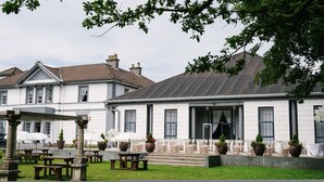 A building with a white facade, large windows, and a covered outdoor seating area with tables and umbrellas. - Room 6 - Manor Park Country House Wales (Swansea)