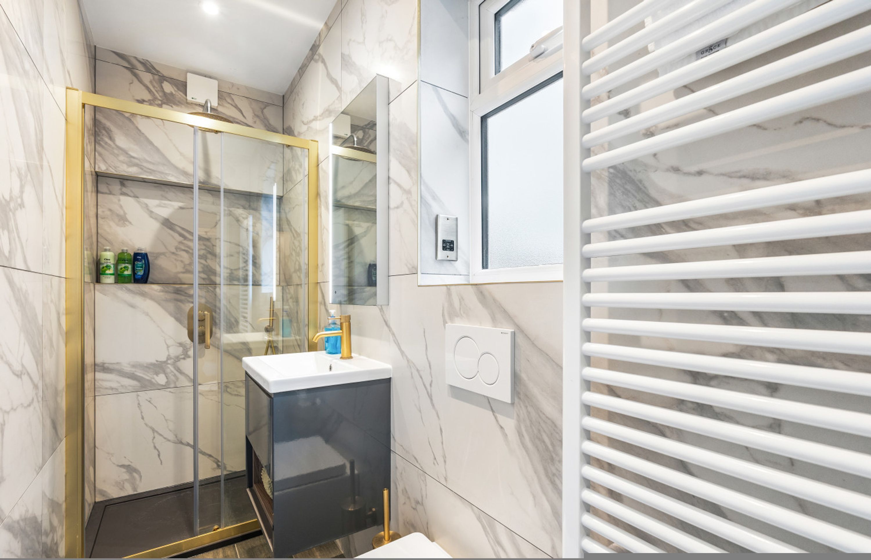 Un baño moderno con cabina de ducha de vidrio, un lavabo blanco y pared revestida de mármol.