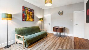 A room with a green sofa, a round wooden table, a colorful abstract painting, a floor lamp, and a ceiling light fixture. - Spacious 5BR Home With Parking in Central Horsham (Horsham)