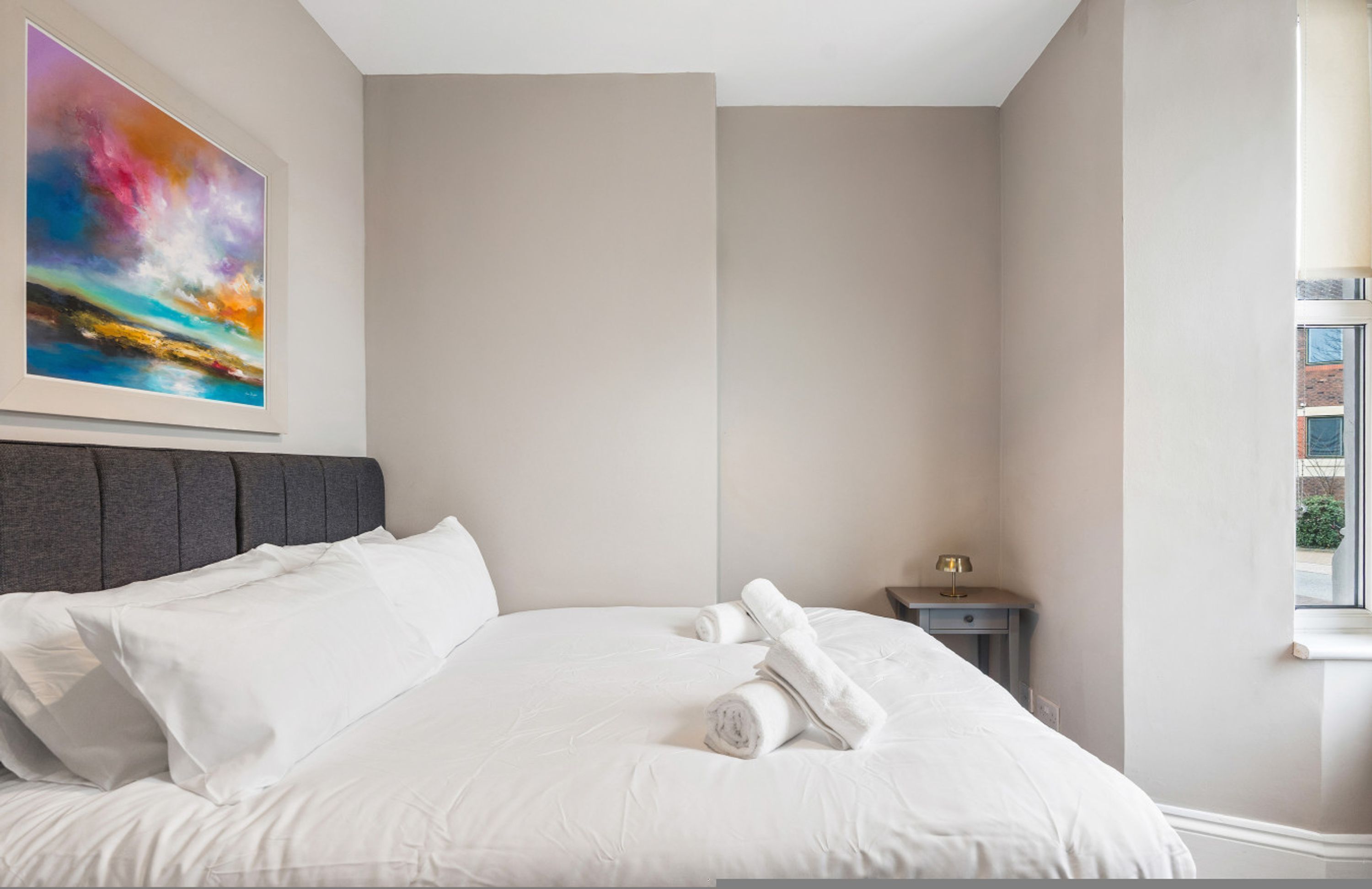 Una camera d'albergo con un letto, un comodino, un quadro e una finestra.