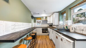 A modern kitchen with a marble backsplash, wooden bar stools, and a large window. - Spacious 5BR Home With Parking in Central Horsham (Horsham)
